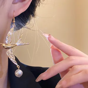 Primo piano di un orecchino vintage a forma di rondine dorata con perla.