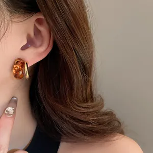 Close-up of Maillard style amber resin and gold-plated geometric stud earrings on ear.
