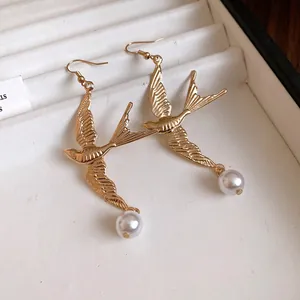Primo piano di orecchini vintage a forma di rondine in oro con eleganti pendenti di perle bianche