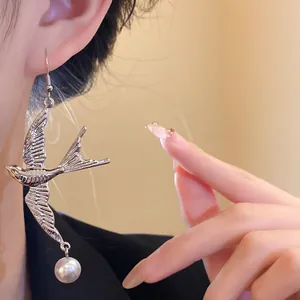 Primo piano dettagliato di un orecchino a rondine in argento con perla indossato sull'orecchio