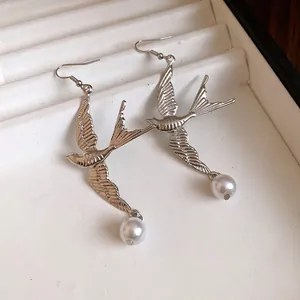 Vista dettagliata di orecchini a forma di rondine in argento con perle lucenti.