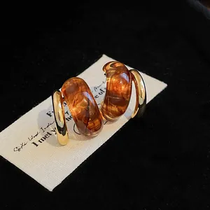 Close-up of amber resin and gold-plated geometric hoop earrings in Maillard style.