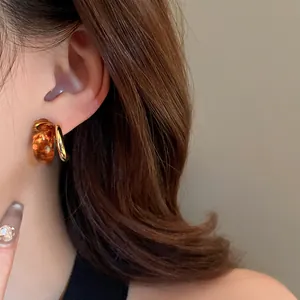 Detailed close-up of Maillard style amber resin and gold hoop earrings worn on an ear.