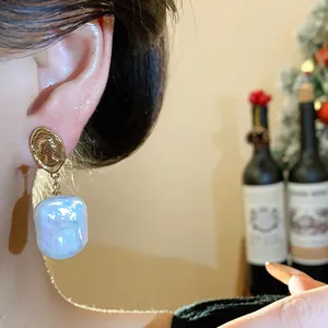 Dettaglio ravvicinato di eleganti orecchini con perle barocche e perno a moneta dorata