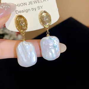 Primo piano dettagliato di eleganti orecchini a medaglione dorati 18k e perle barocche