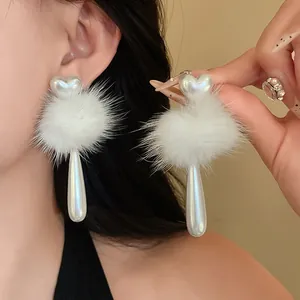 Close-up of elegant heart faux pearl earrings with white pom-pom and teardrop charm