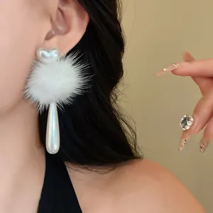 Close-up of white heart faux pearl earrings with fur pom-pom on an Asian model
