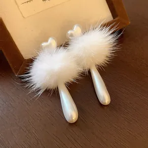 Detailed macro view of white heart pearl earrings with fluffy pom-poms and teardrop drops