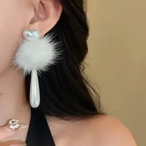Detail of white faux fur ball earrings with heart pearl and teardrop drop on model