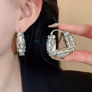 Close-up detail of silver U-shaped earrings encrusted with clear baguette crystals.