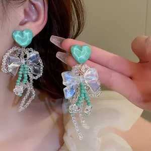 Detailed view of elegant green heart stud earrings with iridescent bow and bead tassels.
