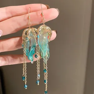 Close-up detail of teal jellyfish tassel earrings with gold chains and blue crystals