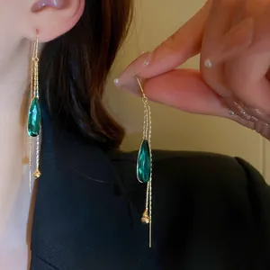 Close-up of elegant long tassel earrings with green teardrop crystal and gold chains.