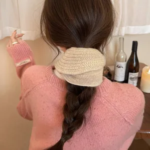 Detailed macro view of a cozy beige knitted large hair scrunchie on a braided low ponytail.