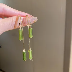 Close-up of elegant gold hoop earrings featuring green bamboo-shaped tassel pendants