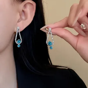 Elegant silver teardrop earrings with turquoise stones and rhinestones worn by a model