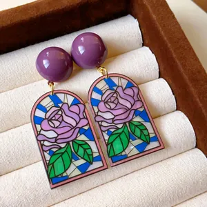 Vue détaillée de boucles d'oreilles vintage avec motif de rose de style vitrail coloré.