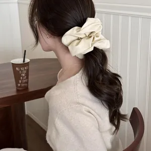 Large beige ruffled scrunchie hair tie shown in a stylish low ponytail hairstyle.