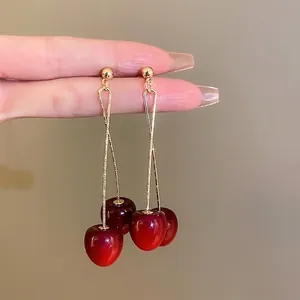 Elegant deep red cherry drop earrings with long slim gold chains shown in hand