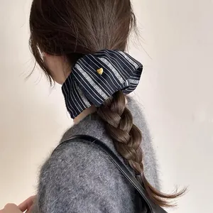 Detail of a vintage striped fabric scrunchie with a gold heart on a braided hairstyle.