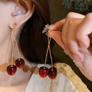Close-up of red cherry drop earrings worn on ear showing glossy finish and gold chain.