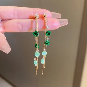 Close-up view of long tassel earrings with green rose charms and pale green beads.