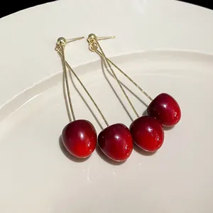 Close-up detail of stylish red cherry pendant earrings with silver needle studs.