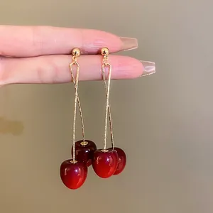 Close-up of trendy red cherry drop earrings with long gold bars
