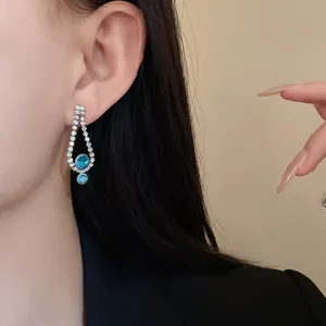 Close-up of elegant silver waterdrop earring with blue gemstones and sparkling rhinestones