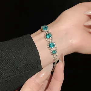 Close-up of elegant silver bracelet featuring teal crystals and rhinestones on a wrist.