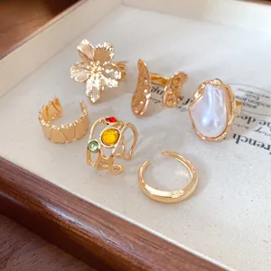 Detalle de anillos dorados estilo vintage con flores, perlas y piedras de colores.