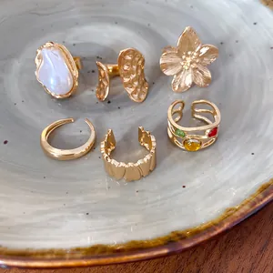 Colección de anillos abiertos texturizados dorados con detalles de flores y perlas