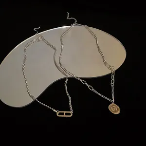 Nahaufnahme von silbernen Schichtketten mit einem H-Glied und einem Münzanhänger-Detail.