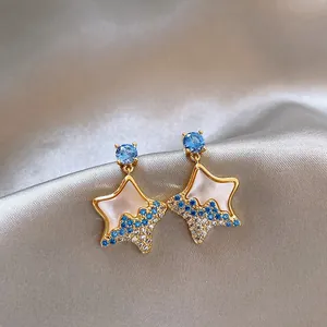 Detailed macro view of gold shell star earrings with blue and white crystals on silk