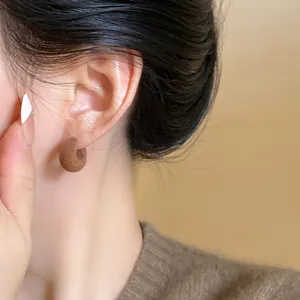Close-up detail showing the texture of a brown flocked C-shaped earring on an ear