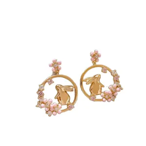 Cute golden bunny earrings with pink flowers and sparkling crystals on white background