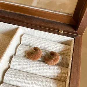 Macro detail of elegant brown flocked C-shaped earrings with S925 silver needles inside a box