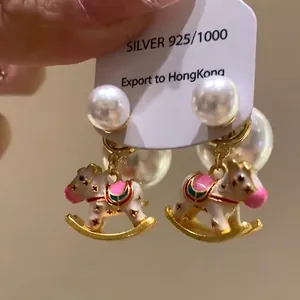 Close-up of cute enamel rocking horse earrings with large white pearls and silver needles