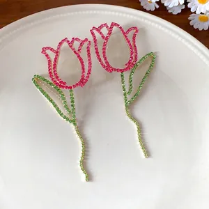 Elegant hollow tulip tassel earrings with pink and green rhinestones on white plate.