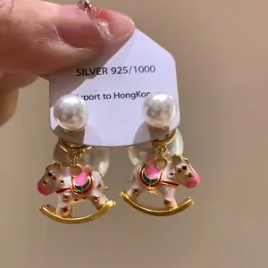 Detailed macro view of 925 silver needle enamel rocking horse and pearl drop earrings