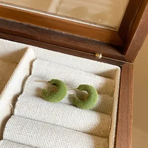 Close-up of green flocked C-shaped stud earrings resting in a wooden jewelry box display