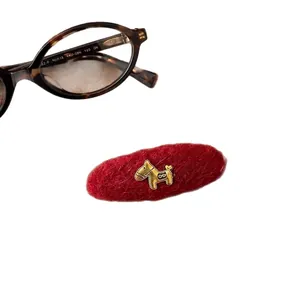 Red flocked BB hair clip with gold horse charm next to tortoiseshell glasses on white background