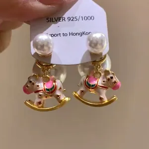 Close-up detail of lovely enamel rocking horse charm and pearl stud earrings on card