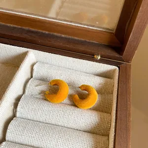 Close-up detail of yellow flocked C-shaped stud earrings featuring a soft velvet texture