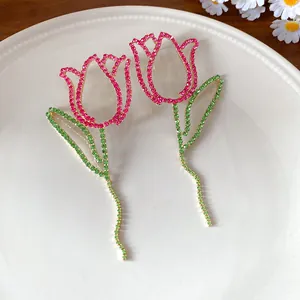 Close-up of hollow rose fringe earrings with sparkling pink and green rhinestones.