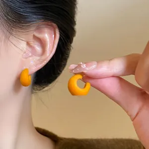 Close-up of orange flocked C-shaped stud earrings worn on the ear and held by a hand