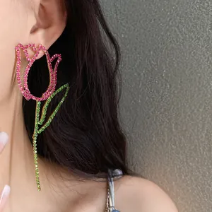 Close-up of exaggerated hollow rose earrings with pink and green rhinestones on ear.