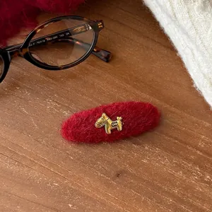 Close-up of a red flocked hair clip with a gold horse charm on a warm wooden background