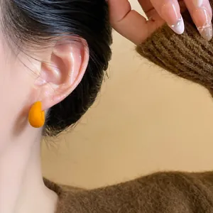 Macro detail view of orange flocked C-shaped stud earrings worn with a knit sweater.