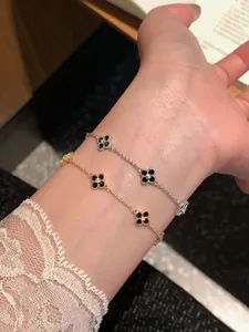 Detail view of two four-leaf clover bracelets on a wrist in gold and silver finish